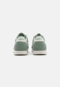 Green suede Reebok sneakers with white accents, featuring a rounded toe, padded collar, and textured rubber sole. Brand logo on heel.