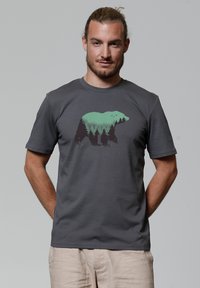 T-shirt en coton gris avec un graphisme représentant un ours entouré d'arbres verts. Manches courtes et col rond. Texture lisse, coupe décontractée.