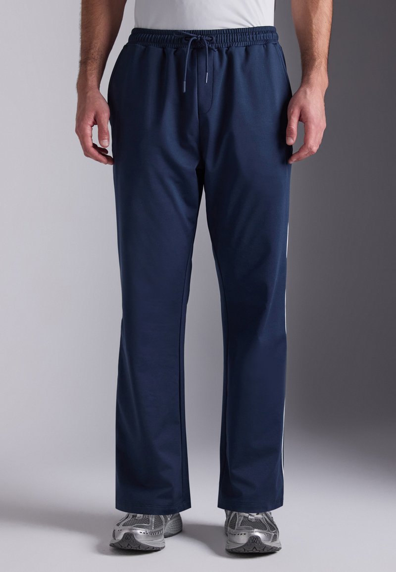 Marineblauwe sportbroeken met een elastische tailleband en trekkoord. Voorzien van een gladde textuur, rechtvallend ontwerp en witte zijstrepen.