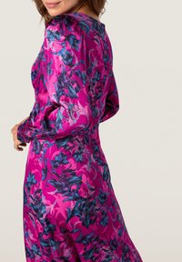 Robe à manches longues en tissu rose vif avec des motifs floraux bleus et violets. Texture lisse avec une silhouette ajustée et des épaules froncées.