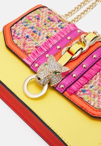 Bolso multicolor con textura tejida, acentos en rosa brillante y naranja, cadena dorada y un detalle de hardware en forma de pantera de strass.