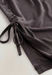 Gros plan sur un tissu gris foncé avec un ourlet cousu et un cordon de serrage noué sur une surface lisse.