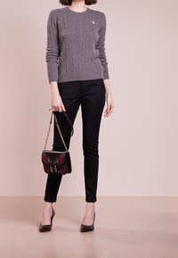 Suéter gris de punto con patrón de trenzas, pantalones ajustados negros, tacones altos negros y un pequeño bolso con acentos florales.