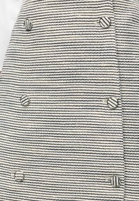 Κοντινό σε μπεζ ύφασμα με οριζόντιες μαύρες ριγέ με κουκκίδες και έξι ταιριαστά στρογγυλά κουμπιά σε δύο κάθετες στήλες.