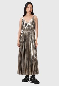 Abito maxi plissettato metallico con scollatura a V e vita elastica, abbinato a calzature nere con dettagli dorati.
