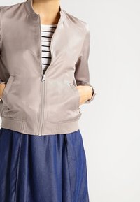 Chaqueta bomber de cuero gris con cremallera frontal, con un cuello redondo, bolsillos laterales y una textura suave, combinada con una falda azul marino.
