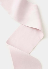 Tissu en lin rose clair plié en courbes douces sur un fond blanc, montrant la texture et les détails du tissage.