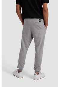 Grey sweatpants made of cotton blend, featuring a back pocket and cuffed ankles. Worn with white sneakers.