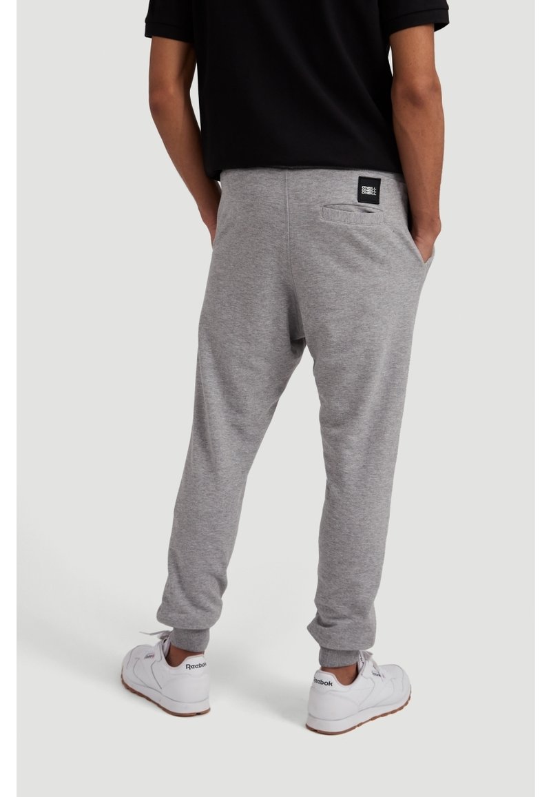 Pantaloni sportivi grigi in misto cotone, con tasca posteriore e caviglie elastiche. Indossati con sneakers bianche.