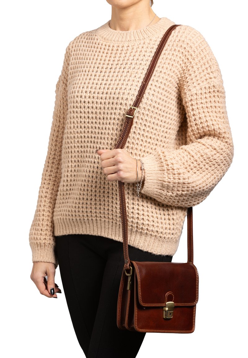 Borsa a tracolla in pelle marrone con una patta, accessori in oro e cuciture bianche, abbinata a un maglione in crema lavorato a maglia e pantaloni neri.