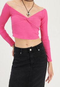 Rosa ribbad crop top med off-shoulder design och långa ärmar, tillsammans med en högmidjad svart denimkjol. Hjärtformad hängande halsband ingår.