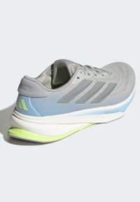 Szare buty sportowe z siateczkową cholewką, zdobione niebieskimi akcentami, z trzema charakterystycznymi paskami, amortyzującą podeszwą środkową oraz jasnoniebieską podeszwą zewnętrzną.