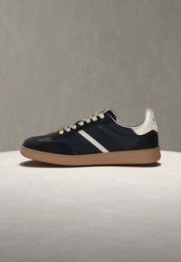 Baskets basses noir et blanc avec des lacets blancs, une semelle gomme et le logo Bally sur le côté et le col du talon.