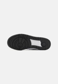 Semelle en caoutchouc noir avec des motifs de grip texturés et un logo Nike blanc. Bords lisses et design de talon arrondi.