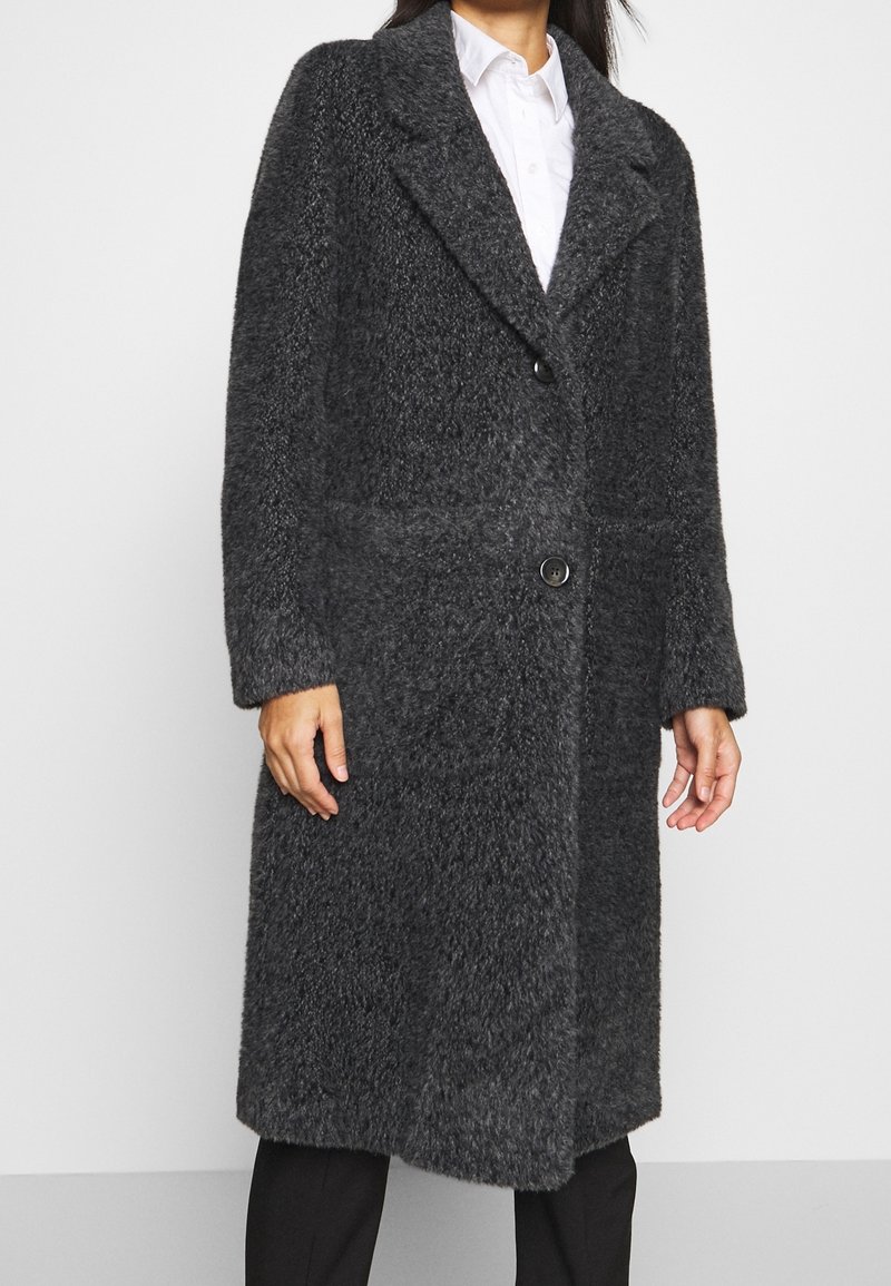 Cappotto grigio e peloso con un design su misura, caratterizzato da una chiusura a bottone, ampie rever e tasche frontali. Le maniche sono lunghe e con una vestibilità rilassata.