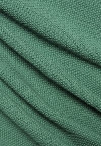 Grüner, strukturierter Stoff mit einem gerillten Muster, der mit drapierten Falten versehen ist und ein weiches, dickes, gestricktes Aussehen betont.