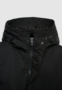 Giacca nera isolata con cappuccio, dotata di chiusura con zip, cordino e dettagli a pressione, texture liscia e fodera interna trapuntata.