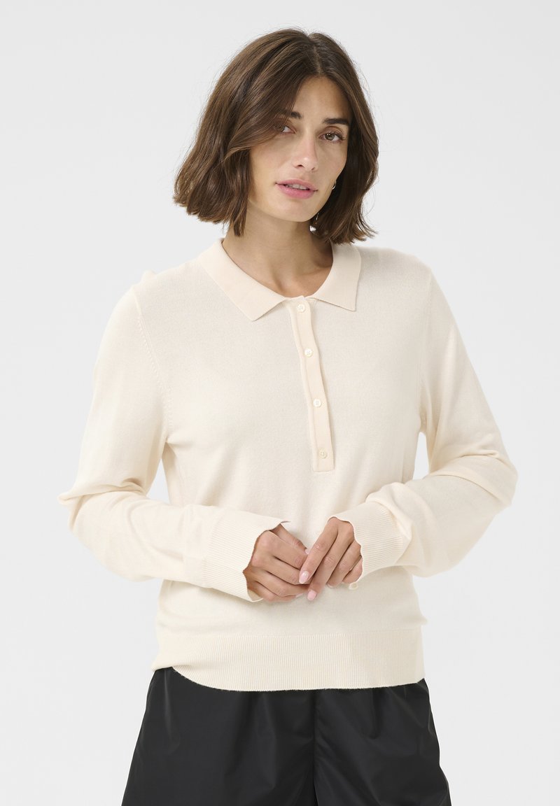 Pulover polo bej deschis cu mânecă lungă, guler, închidere cu butoane și mansete din tricot. Textură moale cu un design ajustat.