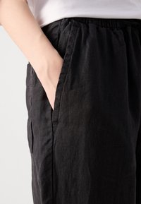 Zwarte linnen broek met een elastische tailleband, voorzien van zijzakken en een relaxte pasvorm. De stof heeft een gestructureerde afwerking.