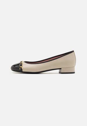 Chaussure pour femme beige à petit talon, bout verni noir et détail chaîne dorée sur le devant, vue de profil sur fond uni.