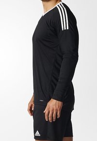 Chemise de sport à manches longues noire avec col blanc et trois rayures blanches sur l'épaule, accompagnée de shorts noirs. Texture lisse.