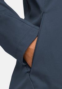 Giacca blu navy con una texture di tessuto liscia, dotata di una tasca laterale e cuciture dettagliate lungo le cuciture.