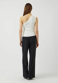 Top blanco de un solo hombro con una silueta ajustada y una textura suave, combinado con pantalones negros de talle alto con pierna recta.
