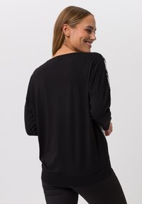 Schwarzes Langarmshirt mit lässigem Schnitt, runder Ausschnitt und grafischen Akzenten an den Ärmeln. Glattes, leichtes Material.