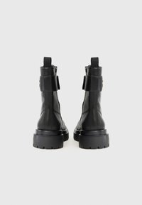 Stivaletti neri in pelle con una texture liscia, suole in gomma spesse e linguette posteriori. Caratterizzati da un design minimalista e cerniere laterali.