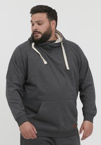 Sudadera con capucha de color gris oscuro en tejido suave, que cuenta con un bolsillo canguro, capucha con cordón en color crema, y puños y dobladillo de canalé. Detalle de etiqueta de marca de piel.