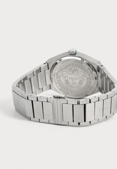 Montre-bracelet en acier inoxydable argenté avec une gravure de tête de Méduse au dos et un bracelet métallique lié fermé sur fond blanc.