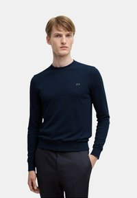 Maglione a maglia navy con maniche lunghe e collo a giro. Presenta un piccolo logo sul lato sinistro del petto. Polsini e orlo a coste.