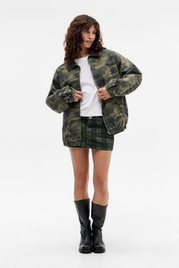 Camo bomberjack met een corduroy kraag, gecombineerd met een groen geruit mini-rokken. Model draagt zwarte kniehoge laarzen.
