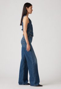 Denim jumpsuit i medium blå, med vide ben og en cropped, ermeløs topp med en frontlomme og justerbare sidelommer.