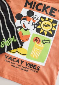 Orange cotton t-shirt featuring a graphic of Mickey Mouse with sunglasses, a drink illustration, and “VACAY VIBES” text. Black striped shorts included.