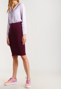 Fialová košile na knoflíky s kapsou, doplněná přiléhavou burgundskou pouzdrovou sukní a růžovými teniskami s oranžovými detaily.