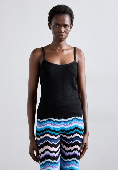 Débardeur noir texturé à fines bretelles, associé à un pantalon à motifs zigzag multicolores dans les tons de bleu, rose et noir.