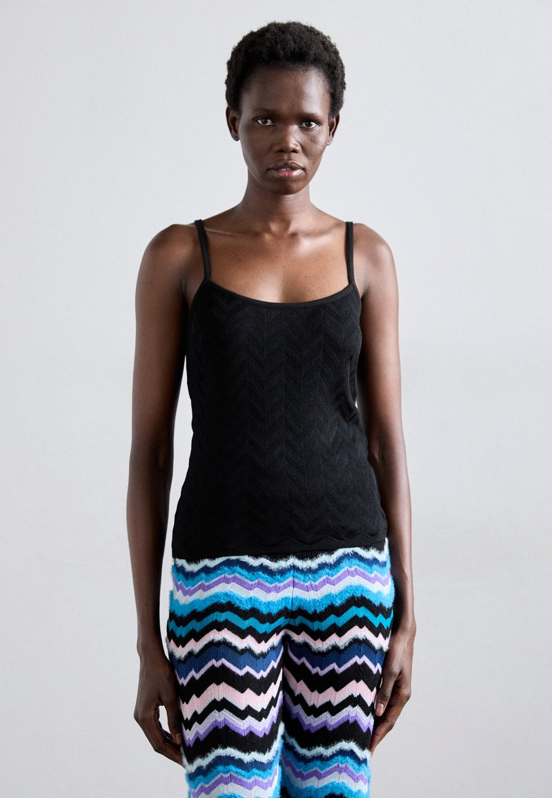 Black, textured tank top with thin straps, paired with multicolored zigzag-patterned pants in blue, pink, and black.