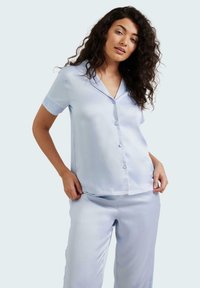 Conjunto de pijama de satén azul claro que incluye una camiseta de botón de manga corta con cuello y pantalones holgados a juego, de textura suave y diseño minimalista.