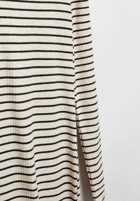 Kermakuvioinen kangas vaaleita vaakaraitoja sisältävällä pitkähihaisella vaatteella, joka on kuvattu yksinkertaisen vaalean taustan edessä.