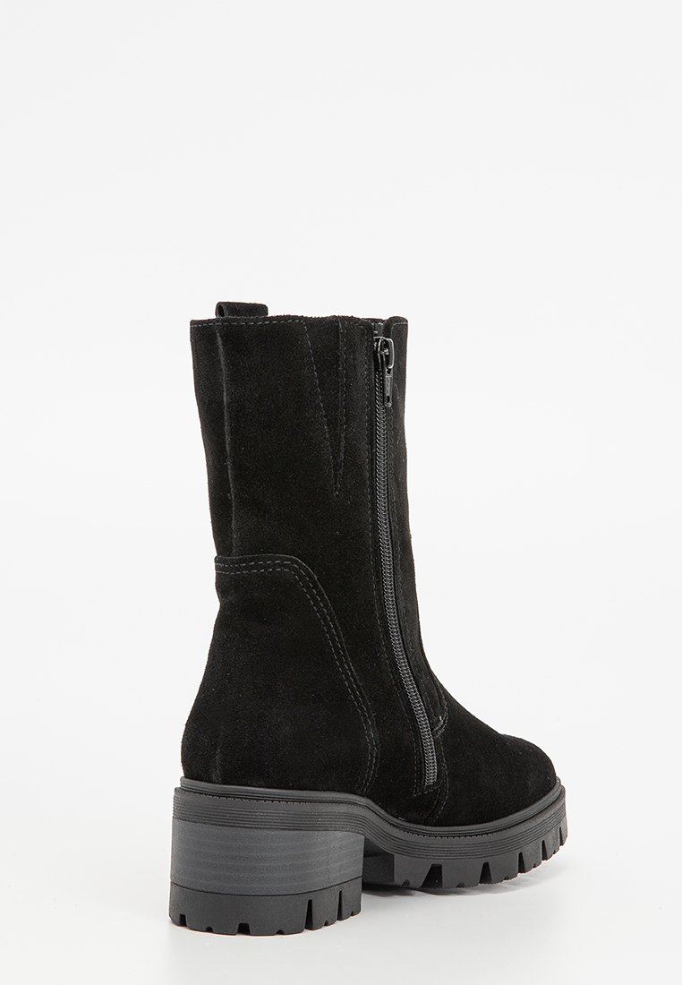 Bottine en suède noir avec une semelle en caoutchouc épaisse et une fermeture éclair sur le côté. Présente un design élégant et des accents cousus le long des coutures.