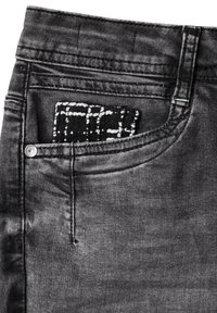 Jeans in denim nero con una texture slavata. La tasca anteriore mostra un tessuto a motivo bianco e nero che spunta. Dettaglio del bottone argentato visibile.