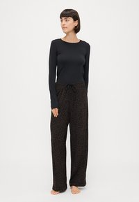 Maglietta nera a maniche lunghe abbinata a pantaloni da pigiama a gamba larga con stampa leopardata marrone, vita con cordoncino e una morbida texture del tessuto.