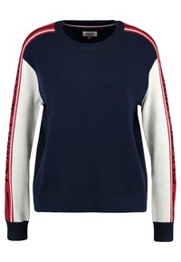 Pull bleu marine avec manches blanches comportant des bandes rouges et le texte "TOMMY". Confectionné en maille douce, col rond et poignets côtelés.