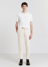 Camicia bianca a maniche corte con colletto a V, abbinata a pantaloni beige chiaro con una leggera texture e stivaletti neri alla caviglia.