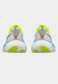 Ζευγάρι λευκών και τιρκουάζ παπουτσιών τρεξίματος με σόλες και λεπτομέρειες σε νέον κίτρινο, εμφανιζόμενα από τη φτέρνα σε απλό φόντο.