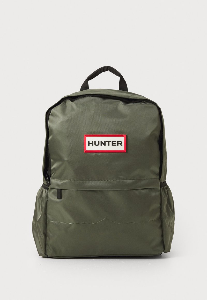 Olajzöld hátizsák elülső cipzáras zsebbel, oldalsó zsebekkel, fekete fogantyúval és a "HUNTER" címkével fehér és piros színben az elülső részen.