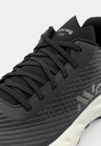 Scarpe sportive nere con superficie texturizzata, caratterizzate da un intricato motivo grigio scuro e lacci robusti. Marchio ben visibile sulla linguetta.