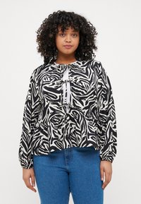 Černobílá halenka s vzorem, dlouhými rukávy, designem peplum a zavázáním na krku. V kombinaci s modrými džíny.