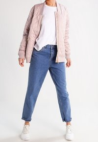 Lyserød quiltet bomberjakke med ribbede manchetter, parret med blå højdelte jeans og hvide sneakers. Enkel, afslappet design.